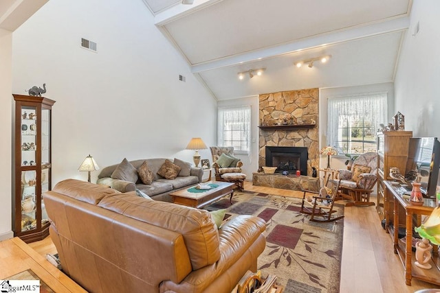 living area featuring high vaulted ceiling, a stone fireplace, wood finished floors, visible vents, and beam ceiling