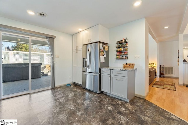 kitchen featuring light stone counters, stainless steel refrigerator with ice dispenser, visible vents, and baseboards