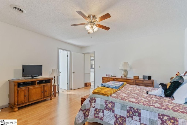 bedroom featuring light wood-style floors, a ceiling fan, visible vents, and a textured ceiling