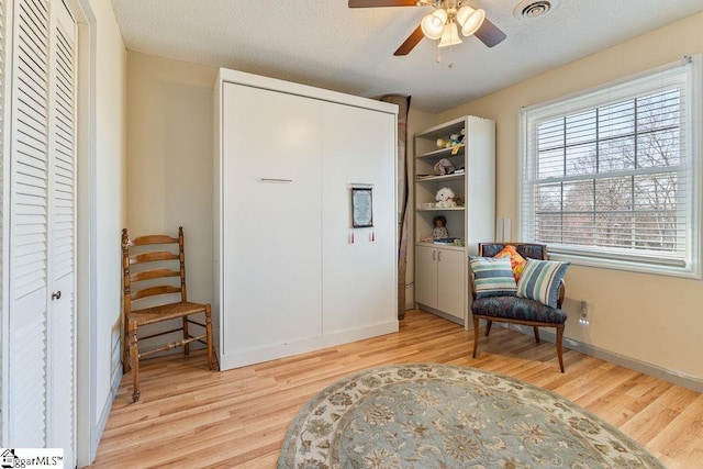 sitting room with light wood-style flooring, visible vents, a ceiling fan, and a textured ceiling