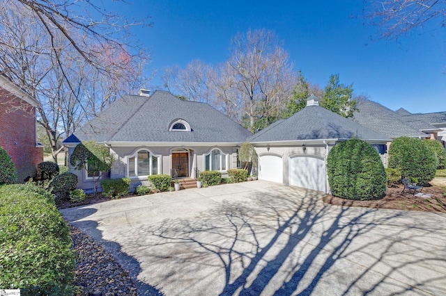 french country home featuring a shingled roof, driveway, a chimney, and an attached garage