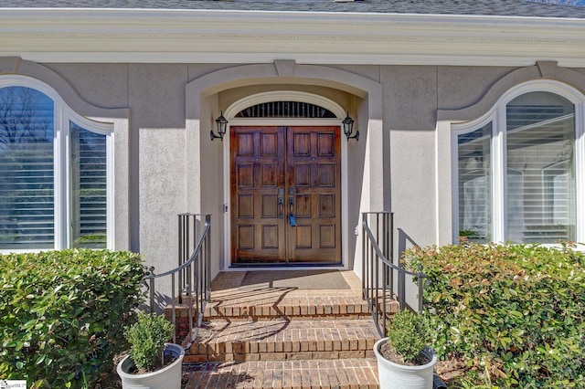 entrance to property with roof with shingles and stucco siding