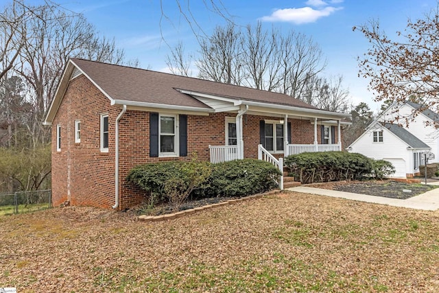 ranch-style home featuring brick siding, a shingled roof, covered porch, fence, and a front lawn