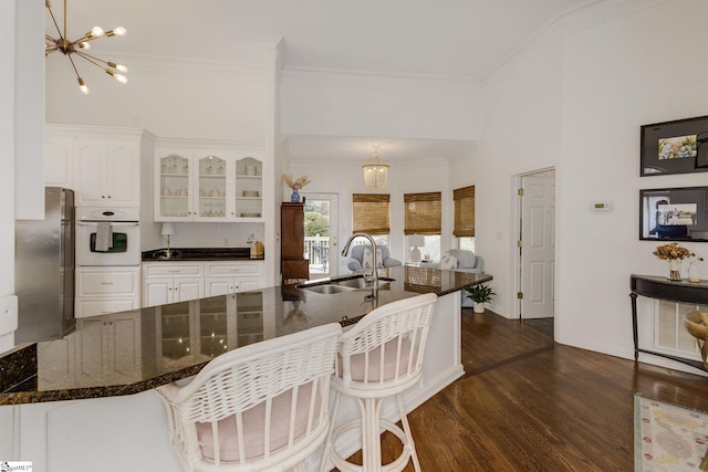 kitchen featuring white oven, an inviting chandelier, freestanding refrigerator, white cabinetry, and a sink