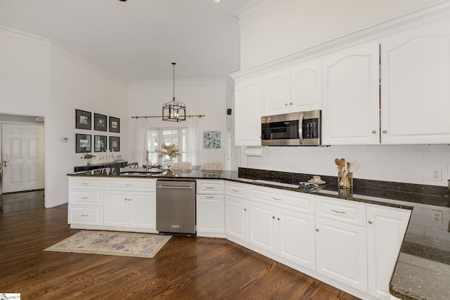 kitchen with dark wood-style floors, a peninsula, stainless steel microwave, and crown molding