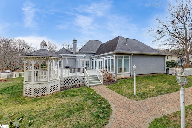 back of property with fence, a deck, a lawn, and a gazebo