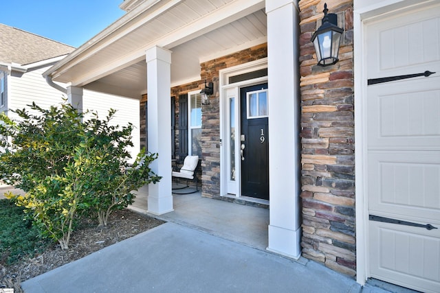 view of exterior entry featuring covered porch, stone siding, and a garage