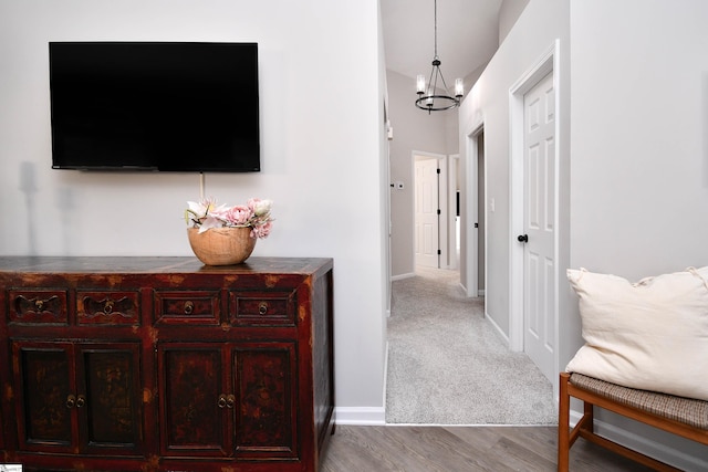 hallway featuring baseboards, carpet floors, wood finished floors, and a notable chandelier