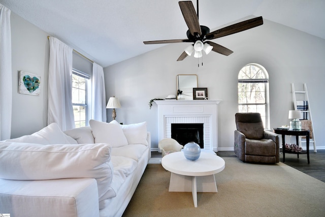 living area featuring lofted ceiling, ceiling fan, a fireplace, and baseboards