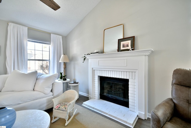 living room featuring lofted ceiling, a brick fireplace, a textured ceiling, wood finished floors, and baseboards