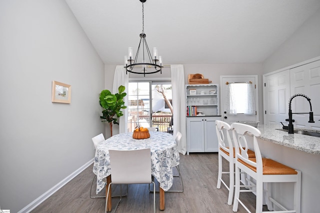 dining space with vaulted ceiling, a notable chandelier, wood finished floors, and baseboards