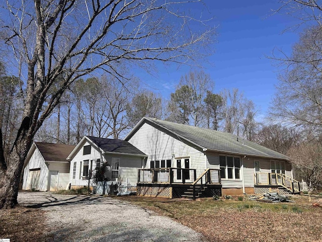 view of side of property with gravel driveway, a wooden deck, and an outbuilding