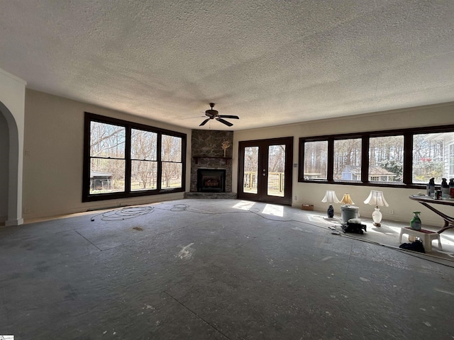 unfurnished living room with a healthy amount of sunlight, a fireplace, arched walkways, and a textured ceiling