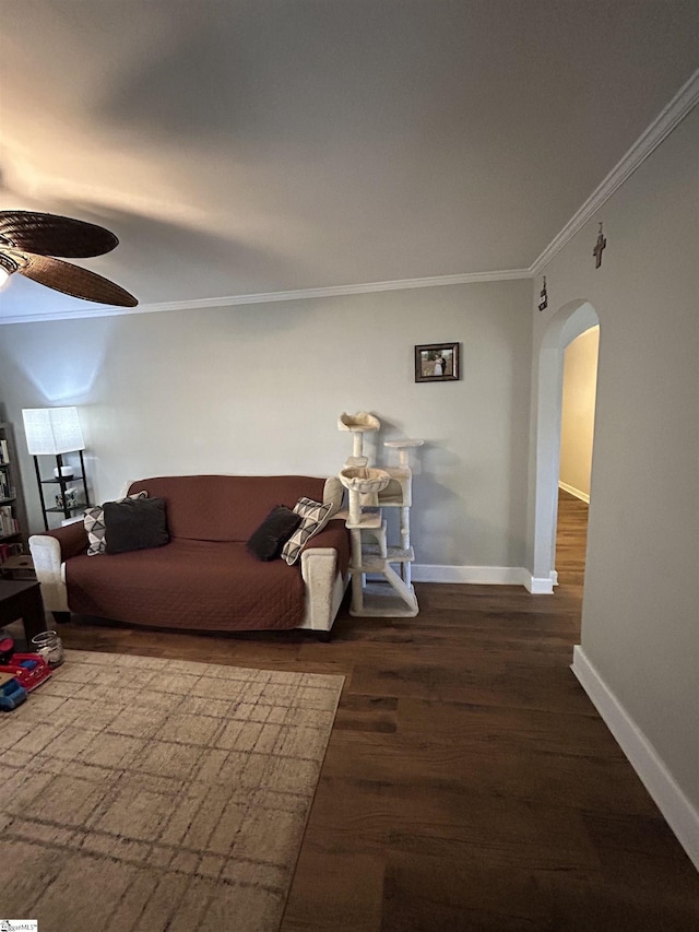 living room featuring baseboards, arched walkways, ceiling fan, ornamental molding, and wood finished floors