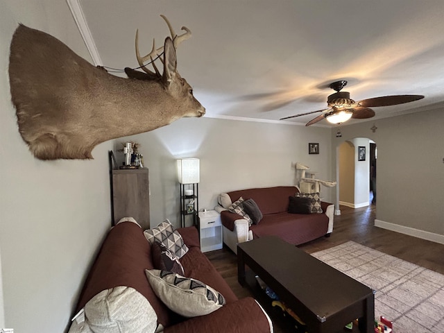 living room with arched walkways, wood finished floors, a ceiling fan, baseboards, and crown molding