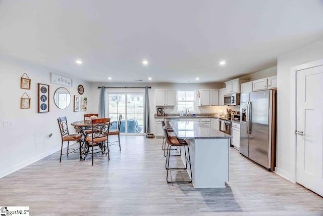 kitchen featuring appliances with stainless steel finishes, a kitchen breakfast bar, a center island, light wood-type flooring, and a sink