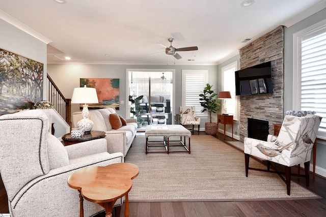 living room with ornamental molding, a stone fireplace, wood finished floors, and a healthy amount of sunlight