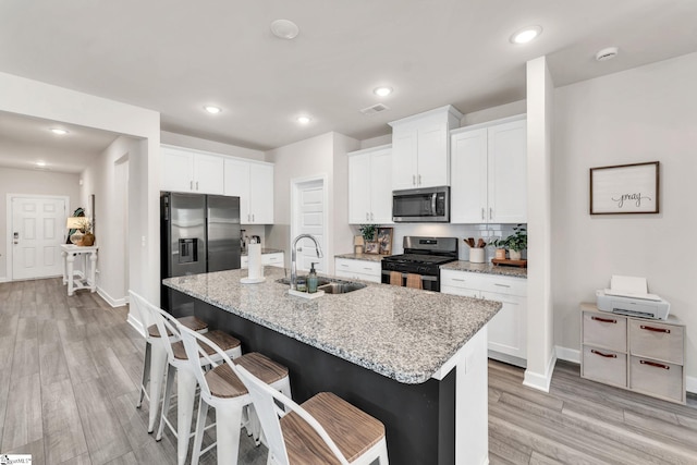 kitchen featuring a kitchen breakfast bar, light stone countertops, stainless steel appliances, white cabinetry, and a sink