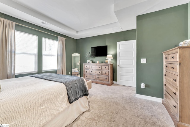 carpeted bedroom with visible vents, baseboards, arched walkways, and a tray ceiling