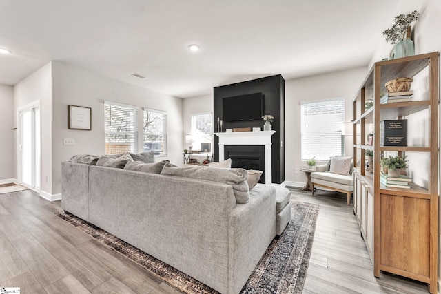 living area with baseboards, recessed lighting, a glass covered fireplace, and light wood-style floors