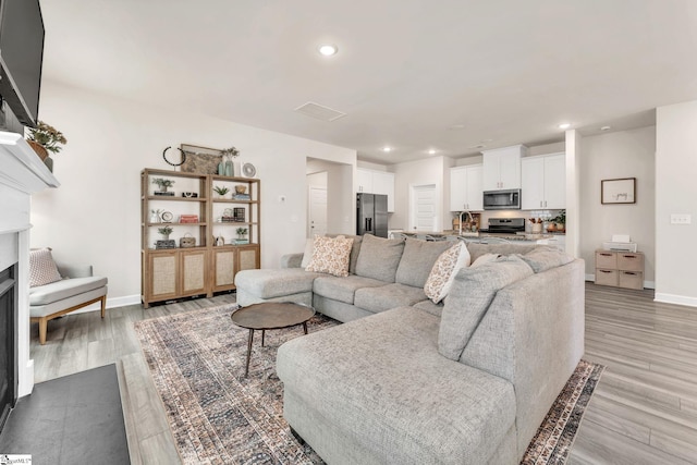 living area featuring light wood-style floors, recessed lighting, a fireplace, and baseboards