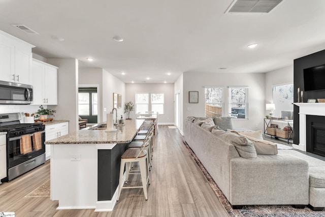 kitchen featuring light stone counters, a sink, white cabinetry, open floor plan, and appliances with stainless steel finishes