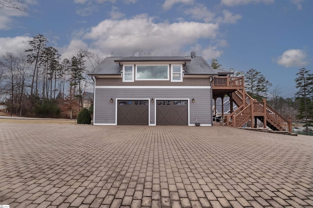 exterior space with decorative driveway, stairway, an attached garage, and a wooden deck