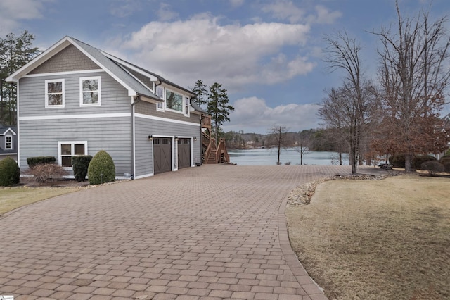 view of side of home with a water view, stairs, a garage, and decorative driveway