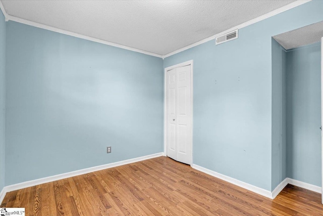 empty room featuring ornamental molding, visible vents, a textured ceiling, and wood finished floors