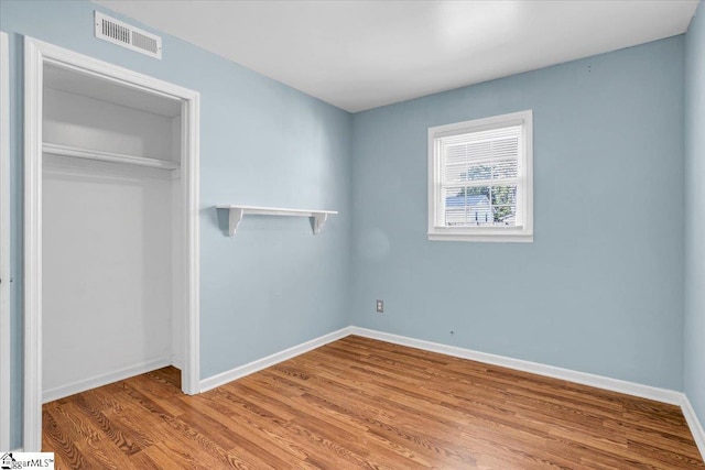 unfurnished bedroom featuring a closet, visible vents, baseboards, and wood finished floors