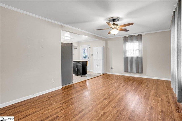 spare room featuring crown molding, baseboards, light wood-style flooring, and a healthy amount of sunlight