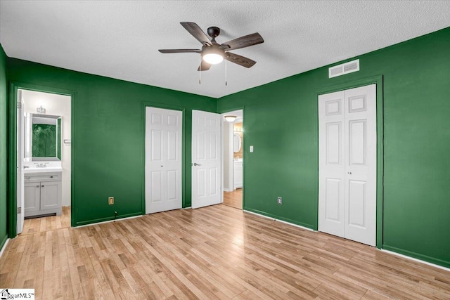 unfurnished bedroom with a textured ceiling, ceiling fan, ensuite bathroom, visible vents, and light wood-type flooring