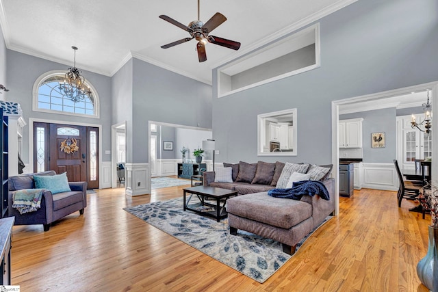 living room with a towering ceiling, a wainscoted wall, light wood-style flooring, and crown molding