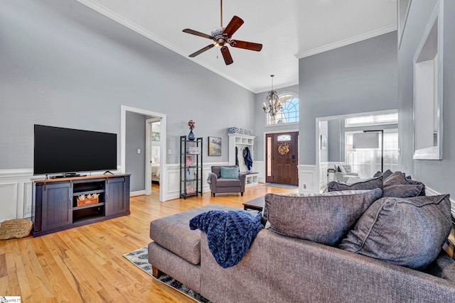 living area featuring ornamental molding, light wood-type flooring, a wainscoted wall, and a towering ceiling