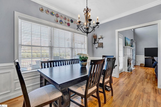 dining space featuring light wood-type flooring, ornamental molding, a decorative wall, and wainscoting