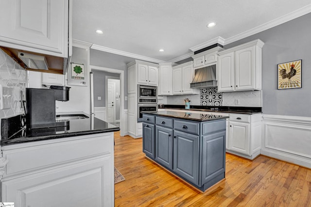 kitchen featuring light wood finished floors, custom exhaust hood, appliances with stainless steel finishes, ornamental molding, and white cabinets