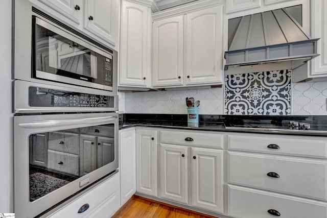 kitchen with stainless steel appliances, tasteful backsplash, custom exhaust hood, and white cabinetry