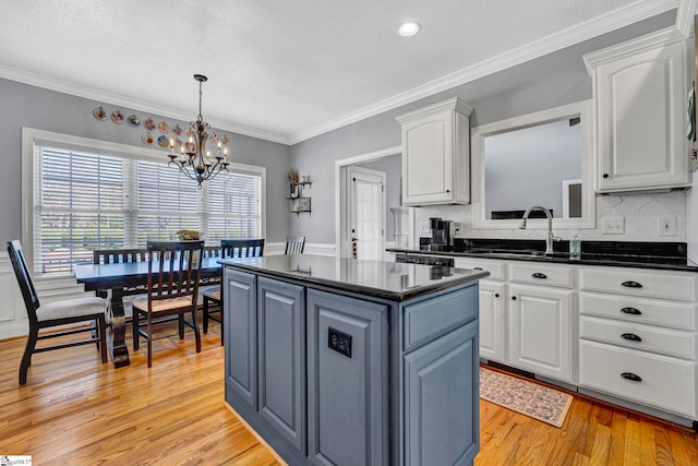 kitchen featuring dark countertops, light wood-style flooring, white cabinets, a kitchen island, and a sink