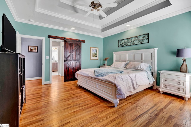 bedroom featuring a tray ceiling, crown molding, light wood-style flooring, a barn door, and baseboards