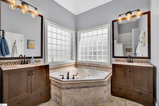 bathroom featuring tiled shower, a jetted tub, two vanities, and a sink