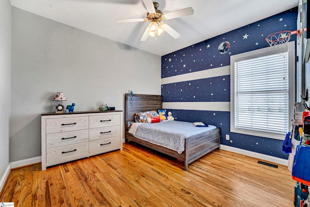 bedroom featuring visible vents, a ceiling fan, wood finished floors, baseboards, and wallpapered walls