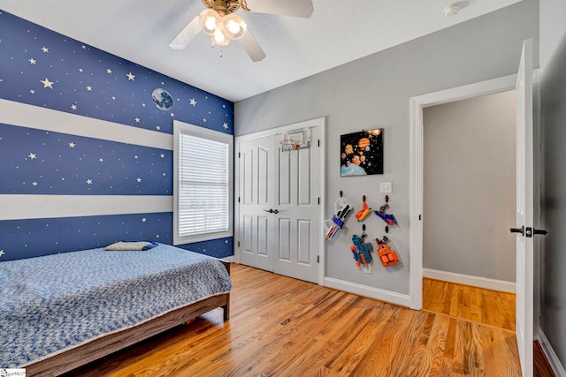 bedroom with wood finished floors, a ceiling fan, baseboards, a closet, and wallpapered walls