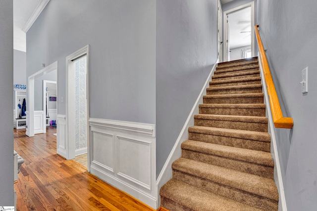 staircase with ornamental molding, wainscoting, a decorative wall, and wood finished floors