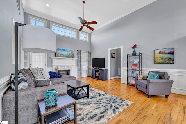 living room with light wood-type flooring, crown molding, a high ceiling, and a premium fireplace