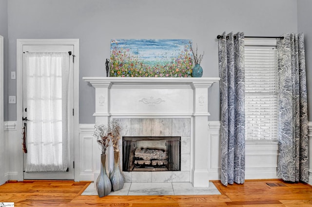 room details with visible vents, wainscoting, wood finished floors, and a high end fireplace