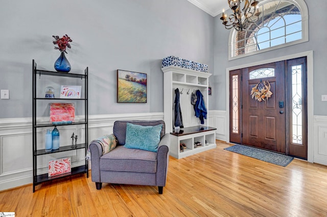 foyer with ornamental molding, a wainscoted wall, an inviting chandelier, and wood finished floors