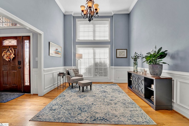 living area with a wainscoted wall, a decorative wall, light wood-style flooring, an inviting chandelier, and ornamental molding