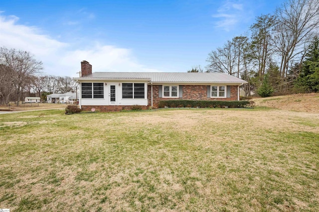 ranch-style house featuring metal roof, a chimney, a front lawn, and brick siding