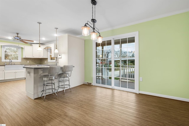 kitchen with crown molding, a breakfast bar area, tasteful backsplash, white cabinetry, and a sink