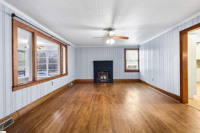 unfurnished living room featuring visible vents, a ceiling fan, wood-type flooring, a lit fireplace, and crown molding